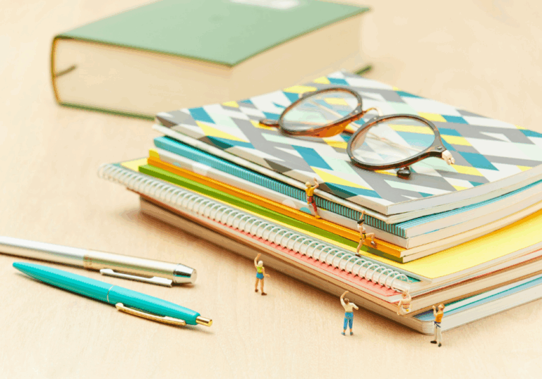 Glasses, notebooks, pens, and tiny people climbing on a table.