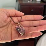 Holding a rhodonite crystal pendant.