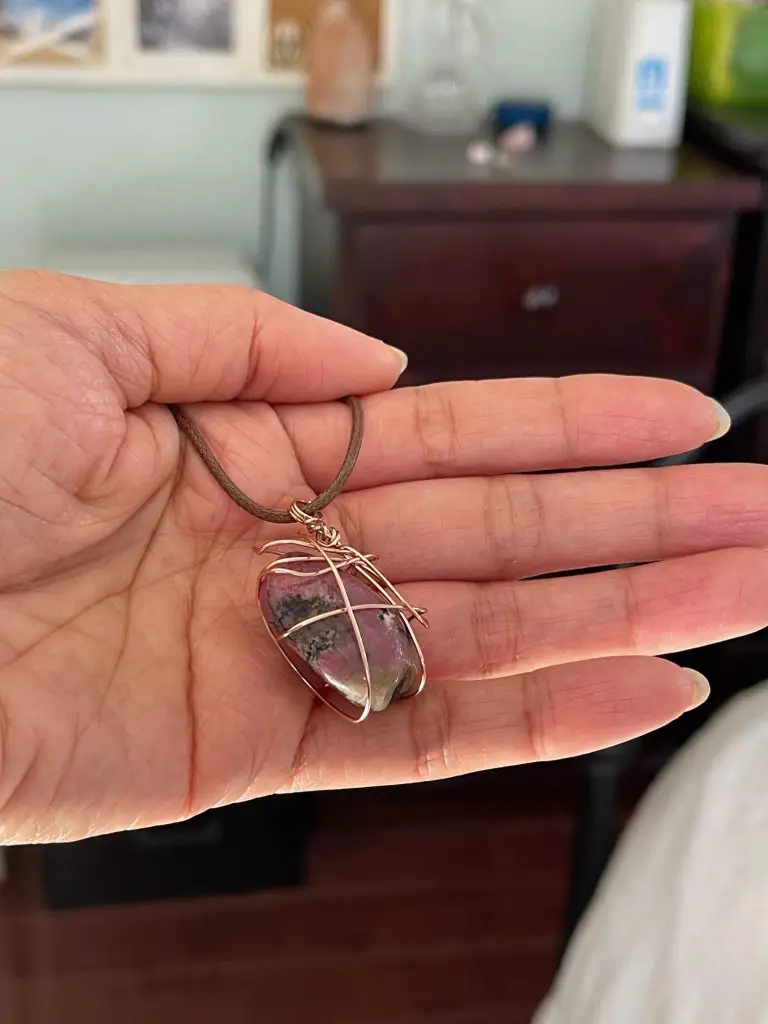 Holding a rhodonite crystal pendant.