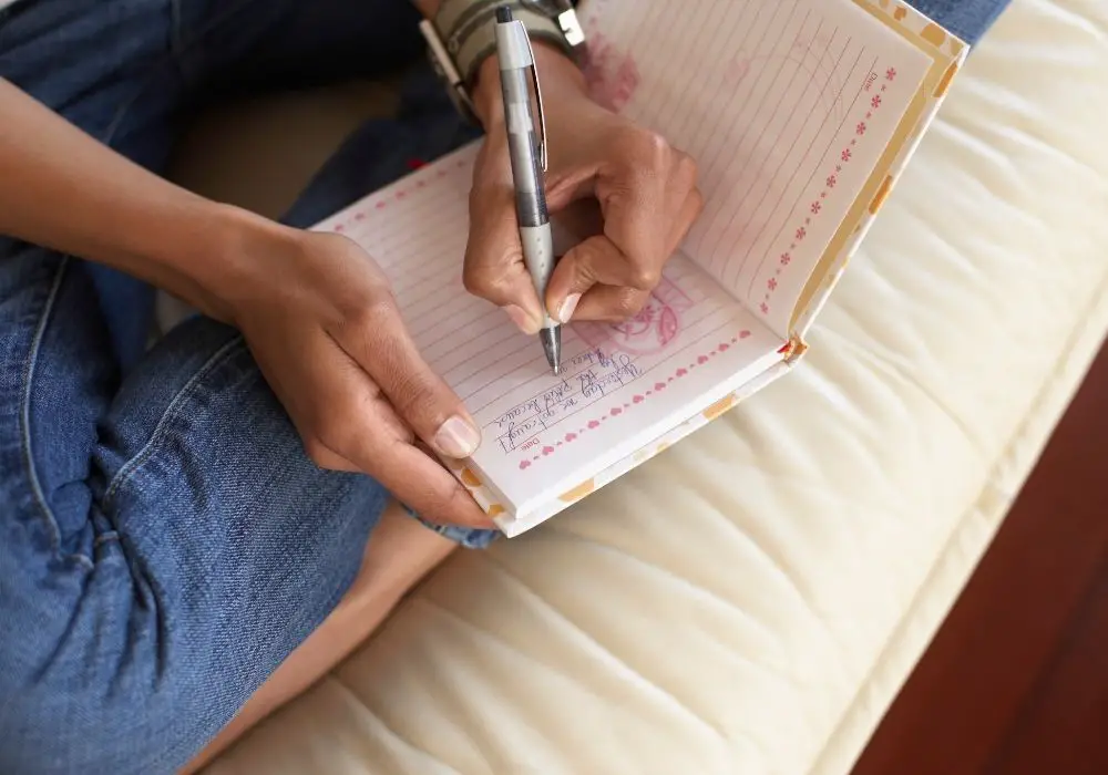Woman writing in her journal while sitting on her bed.