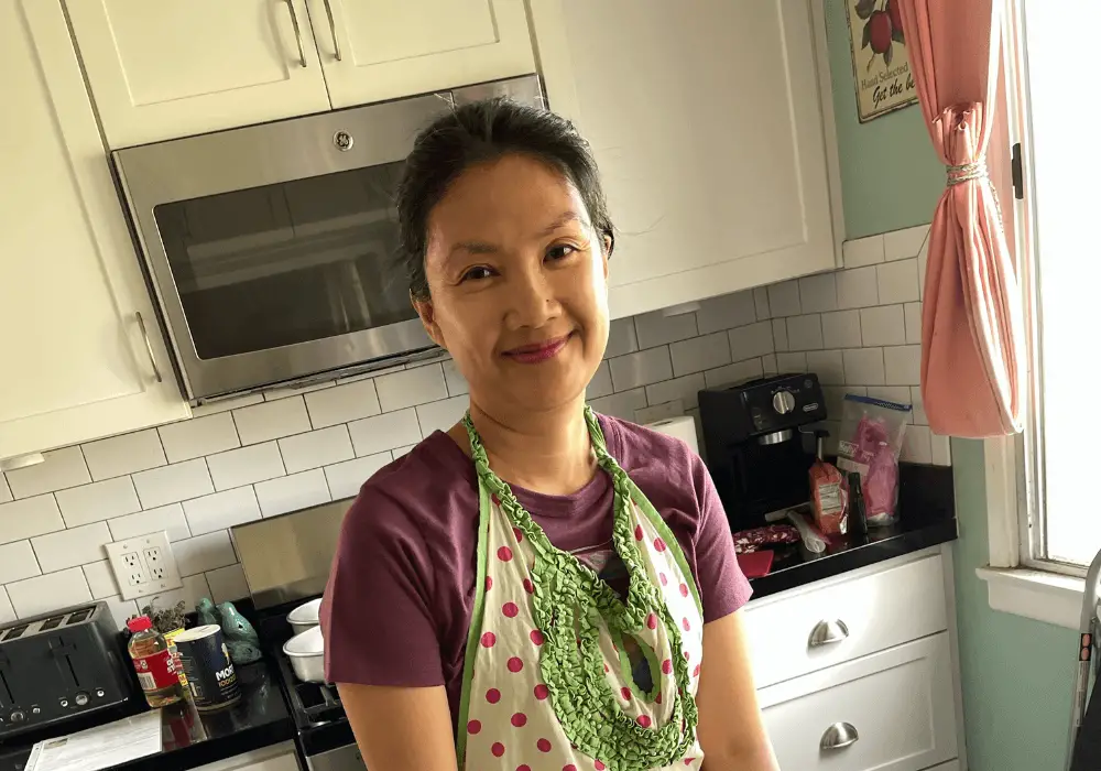 Photo of the author in a colorful apron baking a birthday cake for her husband.