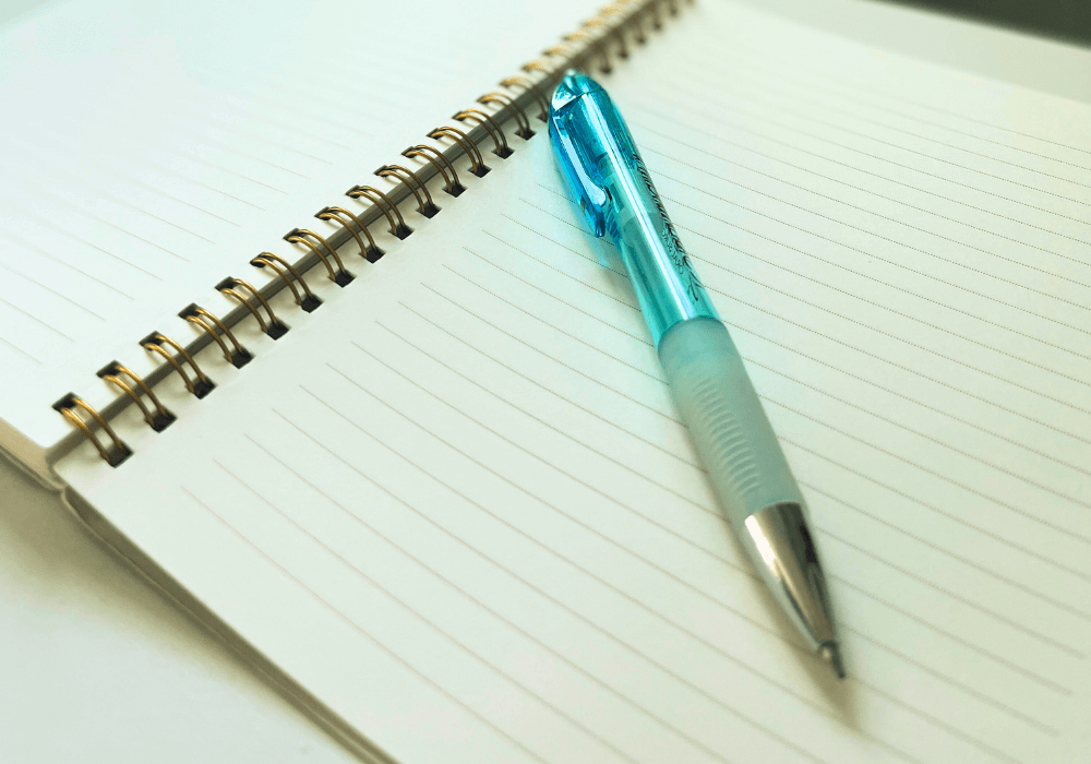 Teal journal pen on a blank notebook page.