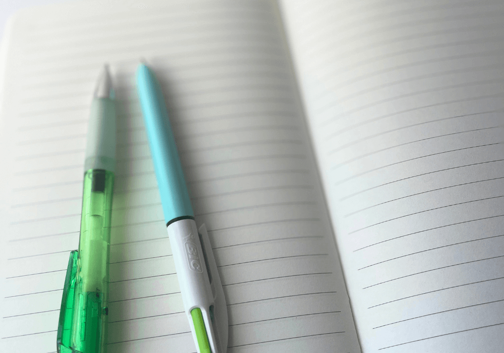 Green gel pen and teal ballpoint pen on a blank notebook page.